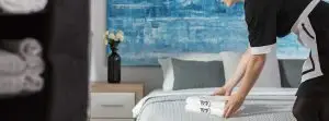 אירועים לעובדים במלונות קיסר פרמייר - עובד מלון במדים מסדר מגבות על מיטה מסודרת בחדר מודרני עם יצירת אמנות כחולה על הקיר.